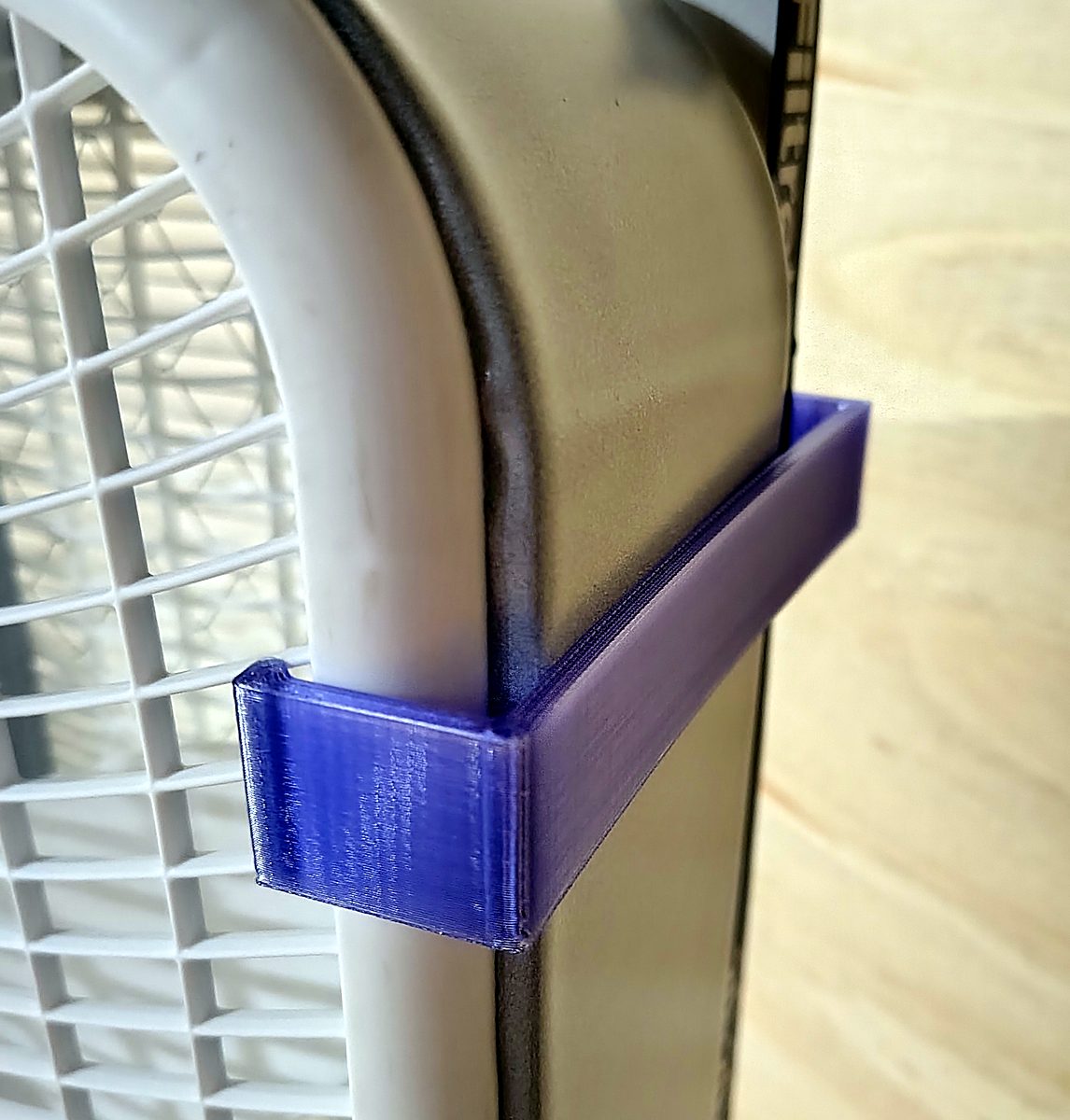 Close-up of one clip: the hook over the fan's rounded rim, the long tab reaching over the filter's border