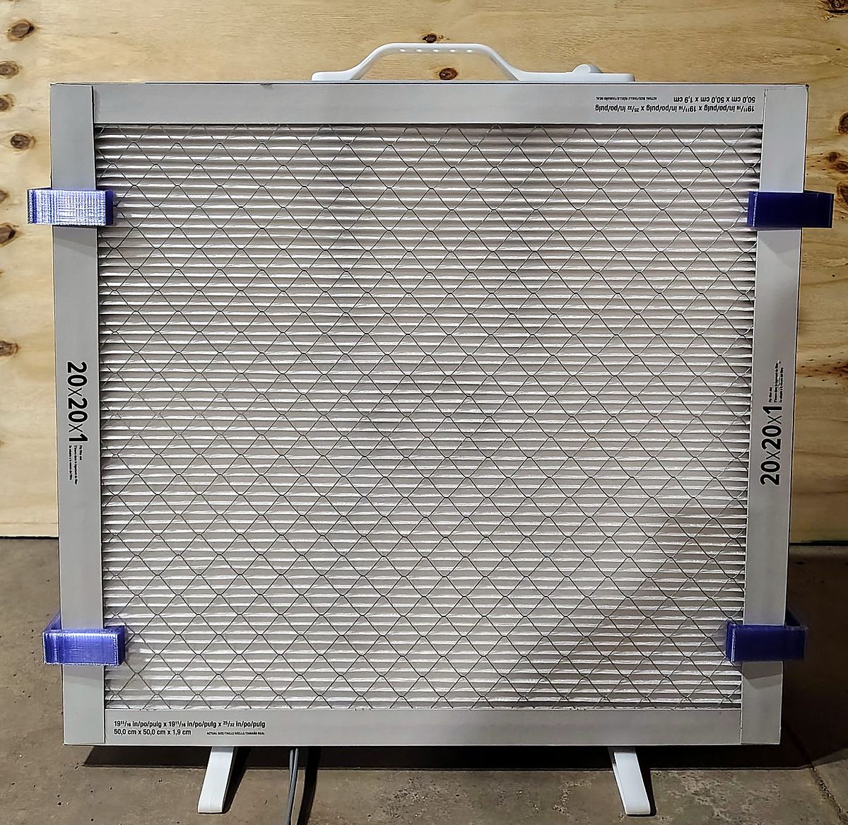 A 20 by 20 furnace filter held on the front of a box fan by translucent purple printed clips at its corners